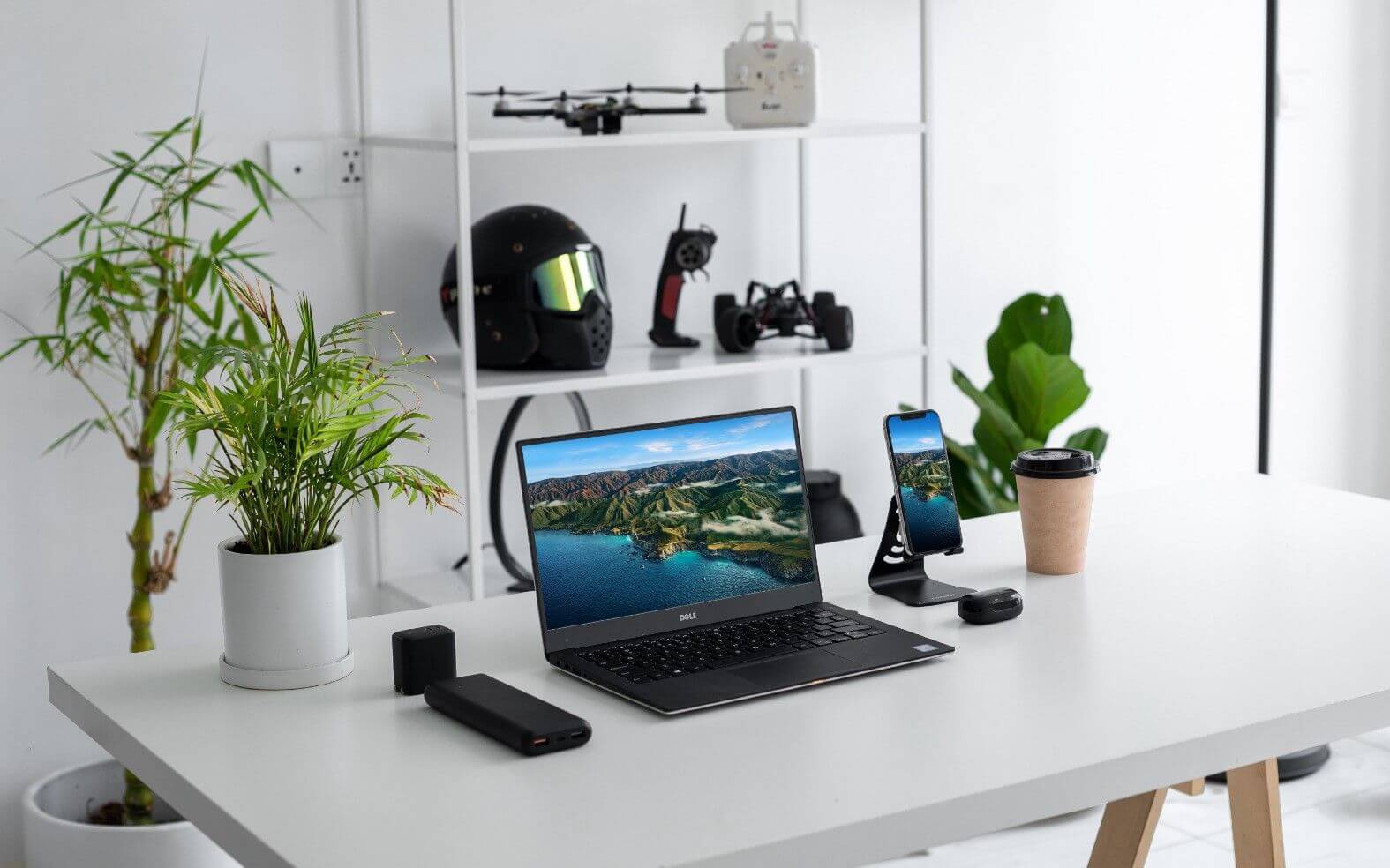 Modern workspace featuring a laptop, smartphone, drone, and indoor plants, emphasizing tech and productivity.
