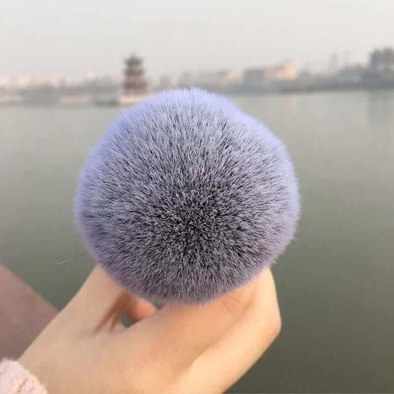 Chubby face makeup brush with soft bristles for seamless foundation application, held against a blurred outdoor background.