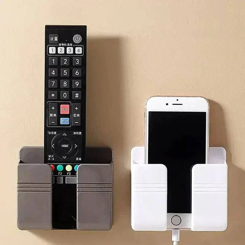 Wall mobile phone holder with remote control and smartphone, features dual compartments for organized storage on light-colored wall.