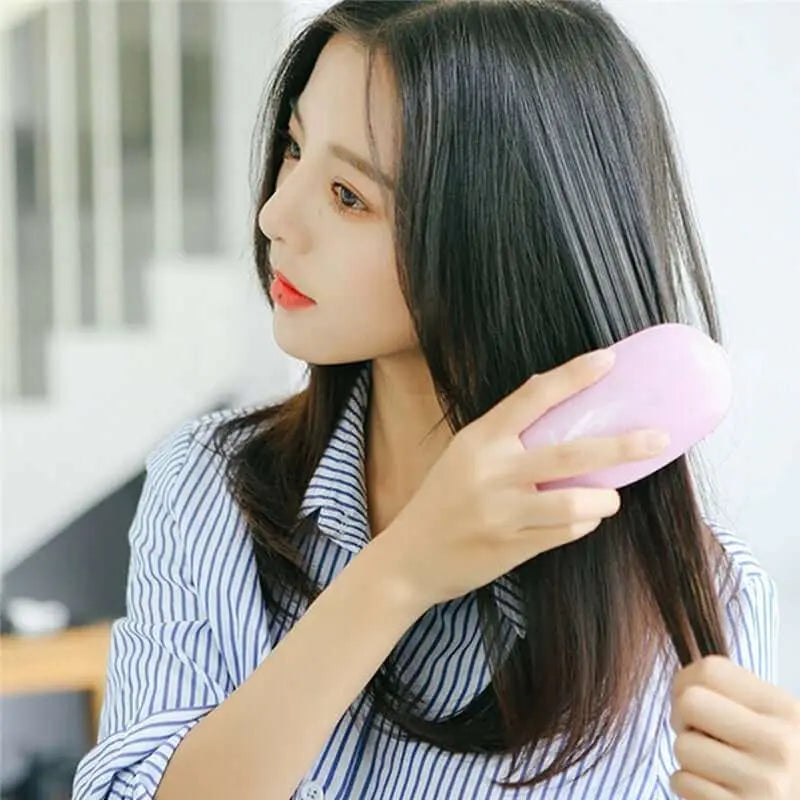 Woman using a portable electric ionic styling hairbrush for smooth and shiny hair.
